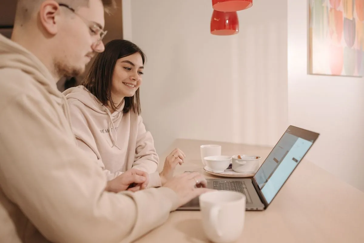 En mann og en kvinne ser sammen på én laptop og smiler, med kaffekopper på bordet